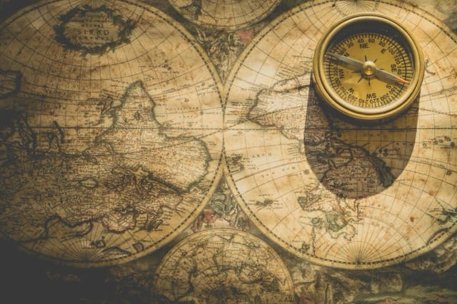 Une carte du monde ancienne en deux hémisphères couleur sépia, avec une boussole de laiton posée dessus. La métaphore de l'essai : une norme de profil professionnel est une carte, ce n'est pas le territoire, et il faut la lire comme telle.