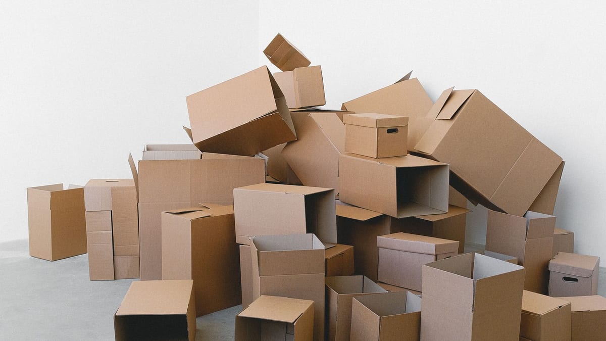 A heap of empty, open cardboard boxes piled in the corner of a bare room with white walls and a concrete floor. The move is over, and nothing is left inside the boxes.