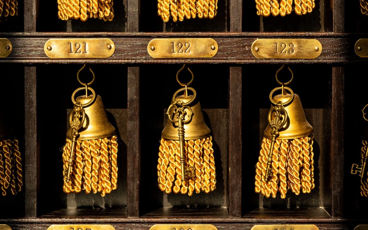 Ein dunkles hölzernes Schlüsselbrett eines Hotels: Messingschilder mit den Nummern 121, 122 und 123, und in jedem Fach ein alter Schlüssel an seinem Haken, mit Ring und goldener Quaste. Jede Autorität hat eine Nummer, einen Platz und einen Haken, von dem man sie abnehmen kann.