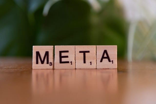 Quattro tessere di legno dello Scrabble allineate su un tavolo compongono la parola «META»; alle spalle, uno sfondo verde sfocato di foglie. Sugli angoli delle tessere si leggono ancora i piccoli numeri del punteggio.